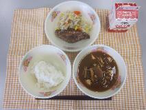 テーブルクロスに並べられた麦ごはん・牛乳・米粉のカレーライス・ひじきと大豆のサラダ・福神漬・ごまドレッシングの写真