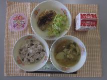 テーブルクロスに並べられた赤はん・牛乳・ゆばのすいもの・チキンハムカツ・ボイルキャベツ・お祝いいちごゼリー・パックソースの写真
