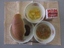 テーブルクロスに並べられたミルクロールパン・牛乳・やさいスープ・ハンバーグのワインソースかけ・フルーツゼリーミックスの写真