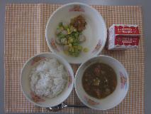 テーブルクロスに並べられた麦ごはん・牛乳・米粉のカレーライス・えだ豆とコーンのソテー・福神漬の写真
