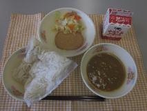 テーブルクロスに並べられたソフトめん・牛乳・米粉のカレーソース・ボロニアソーセージ・コールスローサラダ・コールスロードレッシングの写真