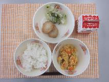 テーブルクロスに並べられたごはん・牛乳・じゃがいものたまごとじ・もち麦入りはんぺん・青菜あえ〔なめしの素〕の写真