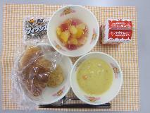テーブルクロスに並べられたクロワッサン・牛乳・米粉のコーンクリームスープ・愛知の大豆入りナゲット・フルーツミックス〔ぶどうゼリー〕・かんそう小魚の写真