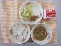 テーブルクロスに並べられた麦ごはん・牛乳・米粉のカレーライス・コーンサラダ・福神漬・コーンドレッシングの写真