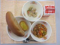 テーブルクロスに並べられたくろロールパン・牛乳・ミートボールのトマト煮・コーングラタン・ツナとやさいのソテーの写真