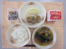 テーブルクロスに並べられたごはん・牛乳・中華スープ・ぶた肉のオイスターソース炒め・りんご・かんそう小魚の写真