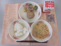テーブルクロスに並べられたごはん・牛乳・かきたま汁・キャベツ入りつくね・ごぼうサラダ・ココア糖・ごまドレッシングの写真