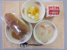 テーブルクロスに並べられた愛知の米粉入りパン・牛乳・かぶの豆乳クリーム煮・メンチカツ・フルーツポンチの写真
