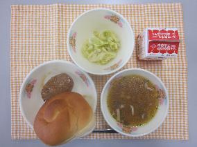 テーブルクロスに並べられたサンドイッチバンズパン・牛乳・コンソメスープ・てりやきハンバーグ・キャベツソテーの写真