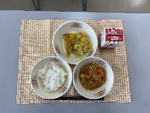 テーブルクロスに並べられたごはん・牛乳・とり肉とやさいのケチャップ炒め煮・スパニッシュオムレツ・フレンチサラダ・フレンチドレッシングの写真