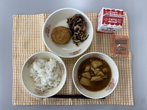 テーブルクロスに並べられたごはん・牛乳・なめこ汁・れんこんサンドカレーフライ・ひじきの煮付け・コーヒー糖の写真