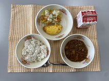 テーブルクロスに並べられた麦ごはん・牛乳・米粉のハヤシライス・オムレツ・コールスローサラダ・コールスロードレッシングの写真
