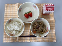 テーブルクロスに並べられたごはん・牛乳・ツナと大豆の煮付け・キャベツ入りメンチカツ（画像なし）・いちごの写真