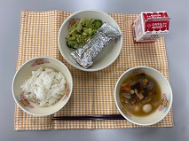 テーブルクロスに並べられたごはん・牛乳・おでん・さんまの銀紙焼き・青菜あえの写真