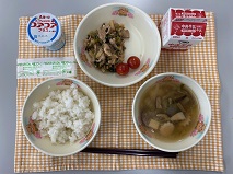 テーブルクロスに並べられたごはん・牛乳・中華スープ・ぶた肉のかき油炒め・ミニトマト・ヨーグルトの写真
