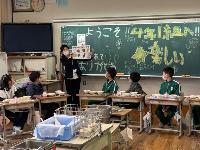 栄養教諭が児童に豊川産の食材のイラストが描かれているボードを見せながら給食に使用している食材の説明をする写真