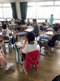 教室の中で給食を乗せた机を円に並べて豊川市長と児童たちがその給食を食べている写真