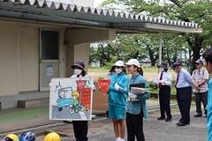 屋外の建物の前で大人たちが止まれの標識とイラストを使って説明している写真