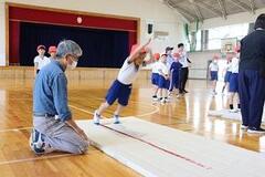 体育館に敷かれたマットに倒れ掛かろうとしている児童の写真
