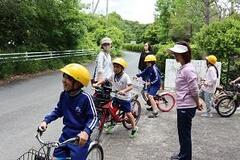 木々の見える道路を自転車に乗った児童たちが走り出そうとしている写真