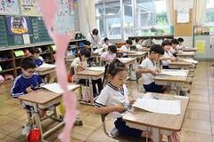 教室の席に座った児童たちが机の上に置かれた用紙にハサミを入れている写真