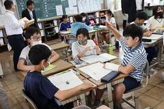 4人一組の席に児童たちが向き合って座り、その中の一人の児童が手を挙げている写真